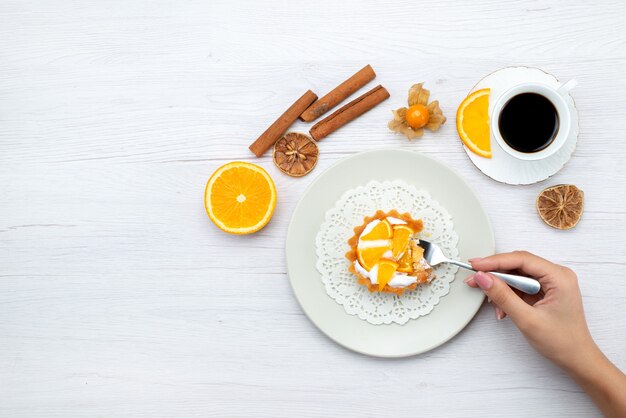 Draußen entfernte Ansicht des kleinen Kuchens mit Sahne und geschnittenen Orangen zusammen mit Kaffee und Zimt auf hellem Schreibtisch, süßem Zucker des Obstkuchenkekses