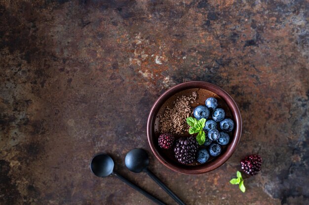 Drei Auflaufförmchen mit Schokoladenmousse mit Heidelbeeren, Brombeeren und frischer Minze auf rostigem Eisenhintergrund