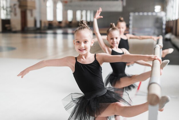 Drei Ballerinamädchen im schwarzen Ballettröckchen, das ihre Beine auf Stange ausdehnt
