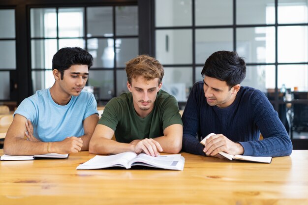 Drei fokussierte Studenten, die zusammen Lehrbücher am Schreibtisch lesen