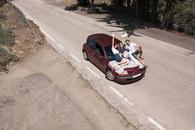 Drei Freunde, die auf der Autohaube genießt die Reise sitzen