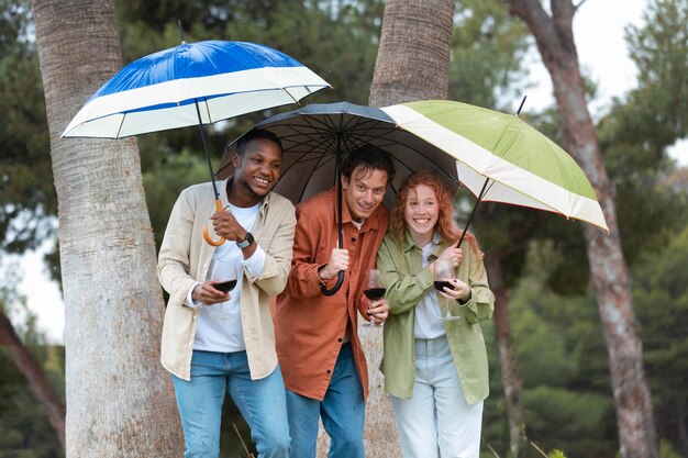 Drei Freunde trinken Wein unter Regenschirmen während einer Party im Freien