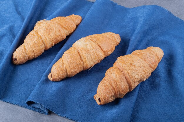 Drei frische französische Croissants auf blauer Serviette.