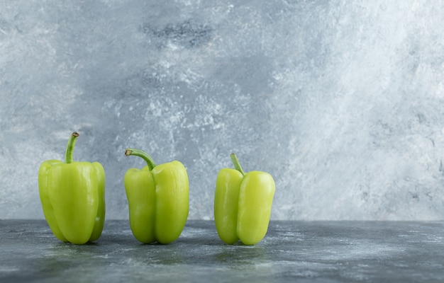 Drei frische organische Gemüsepaprika auf grauem Hintergrund.