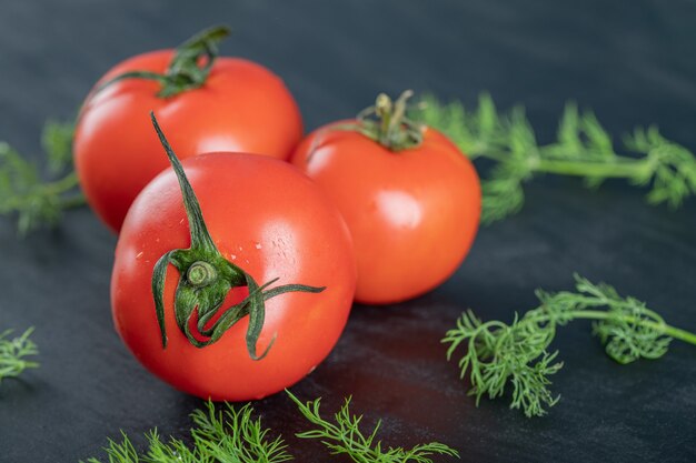 Drei frische Tomaten mit Grüns auf einer dunklen Oberfläche.