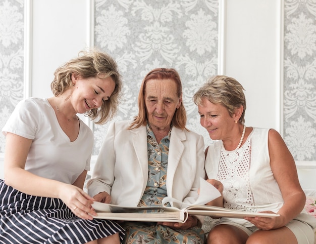 Drei Generationsfrauen, die Fotoalbum beim Sitzen auf Sofa schauen