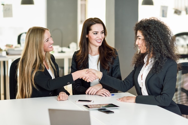 Kostenloses Foto drei geschäftsfrauen händeschütteln in einem modernen büro