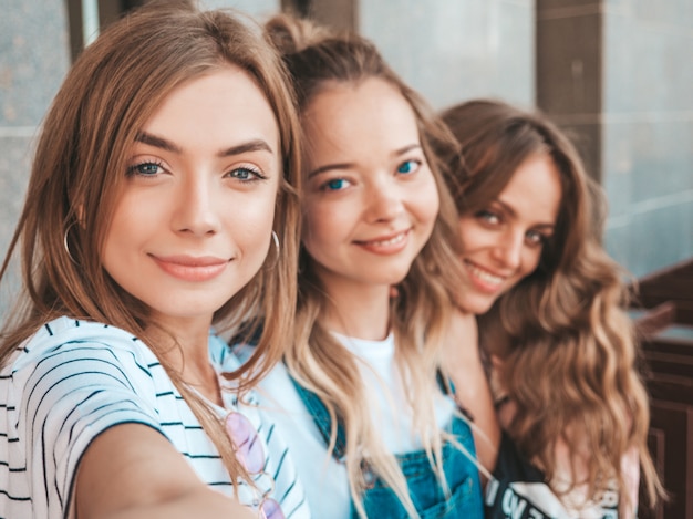 Drei junge lächelnde Hippie-Frauen in der Sommerkleidung Mädchen, die selfie Selbstporträtfotos auf Smartphone machen Modelle, die in der Straße aufwerfen Frauen, die positive Gesichtsgefühle zeigen
