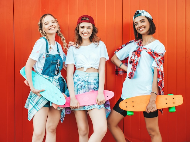 Drei junge lächelnde schöne Mädchen mit bunten Penny Skateboards.