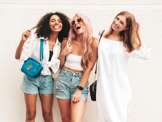 Drei junge schöne lächelnde Frauen in trendiger SommerkleidungSexy sorglose gemischtrassige Frauen posieren auf der Straße HintergrundPositive Models, die Spaß mit Sonnenbrillen haben Fröhlich und glücklich