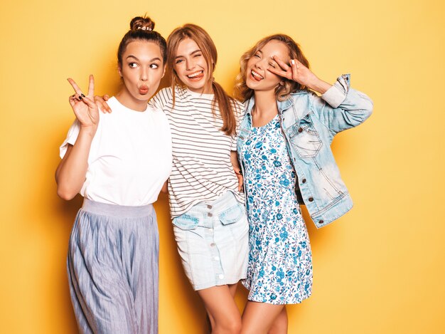 Drei junge schöne lächelnde Hippie-Mädchen in der modischen Sommerkleidung. Sexy sorglose Frauen, die nahe gelber Wand aufwerfen. Positive Models, die Spaß haben