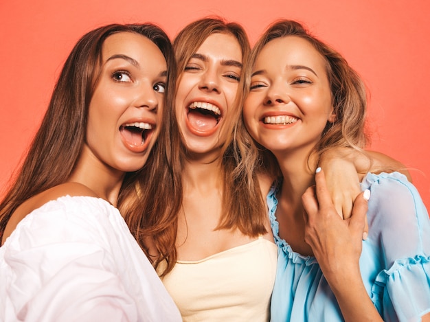 Drei junge schöne lächelnde Hippie-Mädchen in der modischen Sommerkleidung. Sexy sorglose Frauen, die nahe rosa Wand aufwerfen. Positive Modelle, die verrückt werden. Selfie-Selbstporträtfotos auf Smartphone machen