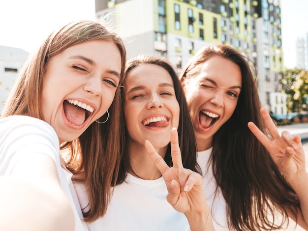 Drei junge schöne lächelnde Hipster-Frauen im trendigen Sommer gleiche Kleidung Sexy sorglose Frauen posieren auf der Straße HintergrundPositive Models, die Spaß mit Sonnenbrillen habenPov-Selfie-Fotos machen