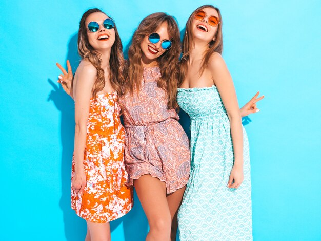Drei junge schöne lächelnde Mädchen in den bunten Kleidern des modischen Sommers. Sexy sorglose Frauen mit Sonnenbrille.