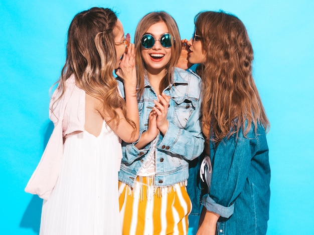 Drei junge schöne lächelnde mädchen in der beiläufigen kleidung des modischen sommers. sexy frauen teilen geheimnisse, klatsch. lokalisiert auf blau.