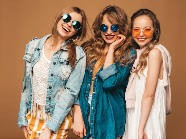 Drei junge schöne lächelnde Mädchen in der zufälligen Jeanskleidung des modischen Sommers. Sexy sorglose Frauenaufstellung. Positive Models in Sonnenbrillen
