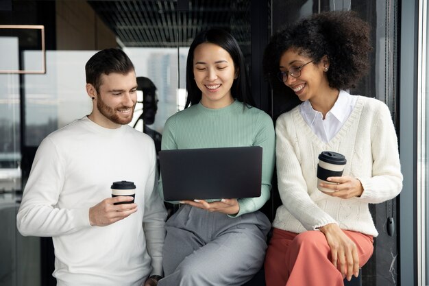 Drei Mitarbeiter, die mit einem Laptop arbeiten und Kaffee trinken