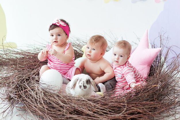 Drei niedliche kleine Babys und Kaninchen mit Ostereiern, die im sehr großen Nest sitzen