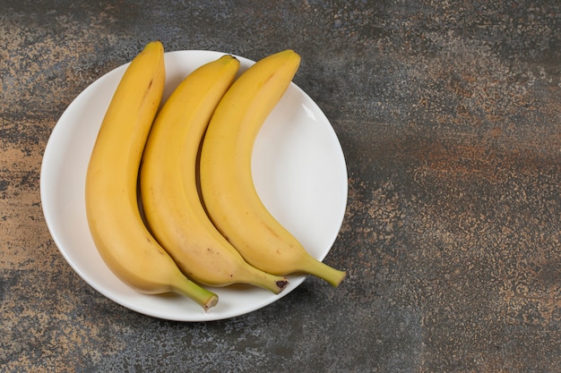 Drei reife Bananen auf weißem Teller.