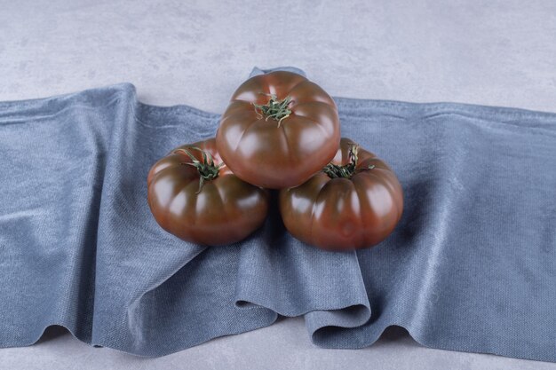 Drei reife Tomaten auf blauem Tuch.