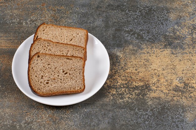 Drei Scheiben Schwarzbrot auf weißem Teller.