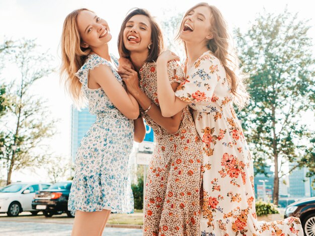 Drei schöne lächelnde Mädchen im trendigen Sommer-Sommerkleid, das auf der Straße aufwirft