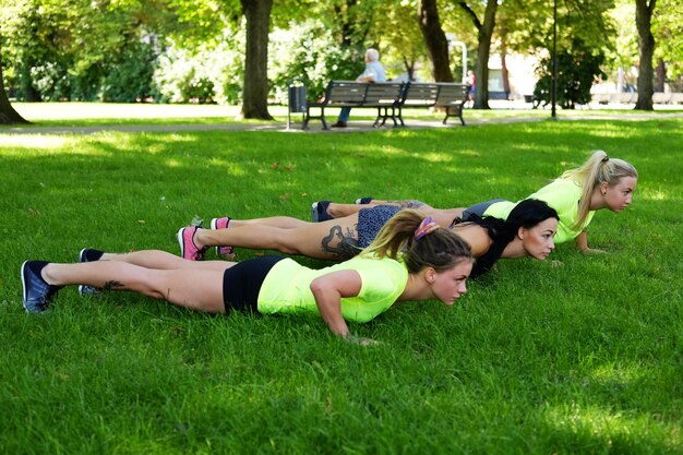 Drei sportliche Frauen wärmen sich auf einer Wiese im Sommerpark auf.