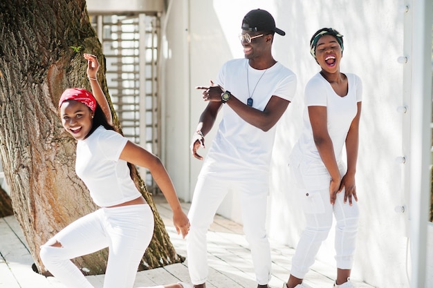 Drei stilvolle afroamerikanische Freunde tragen weiße Kleidung Straßenmode junger schwarzer Menschen Schwarzer Mann mit zwei afrikanischen Mädchen, die Gangsta-Rap-Stil tanzen