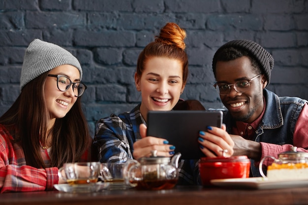 Drei studenten ruhen sich drinnen aus, genießen eine drahtlose internetverbindung im café und nutzen ein elektronisches tablet