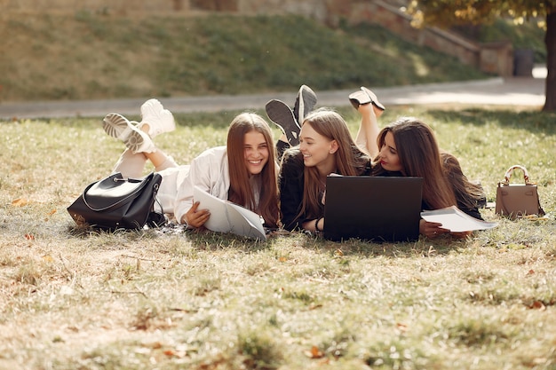 Drei Studenten sitzen auf einem Gras mit Laptop