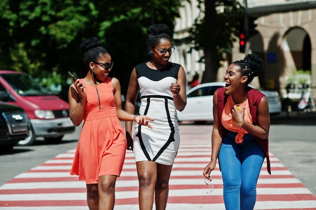 Drei stylische afroamerikanische Frauen, die auf Zebrastreifen oder Fußgängerüberwegen laufen, sprechen miteinander und haben Spaß