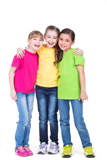 Drei süße kleine süße lächelnde Mädchen in den bunten T-Shirts stehen - lokalisiert auf Weiß.