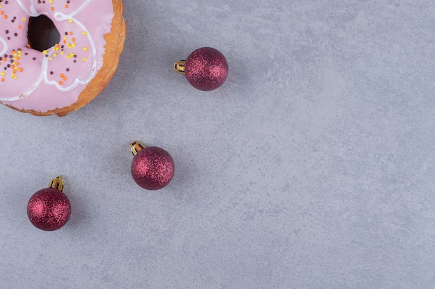 Drei Weihnachtskugeln und ein Donut auf Marmoroberfläche