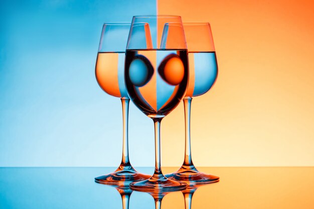 Drei Weingläser mit Wasser über blauem und orange Hintergrund.
