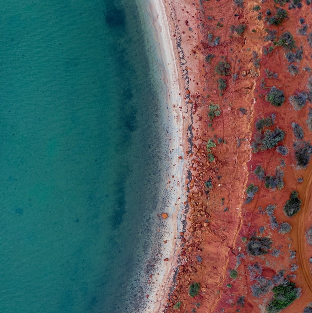 Drohnenblick auf das Meer, umgeben vom Ufer, bedeckt mit rotem Sand und Steinen