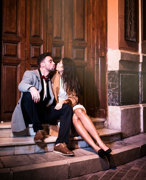 Dünne Frau, die mit jungem Mann küsst und nahe Tür auf Straße sitzt