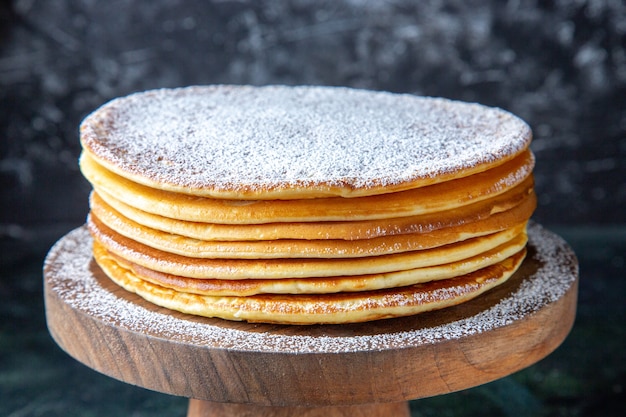 Kostenloses Foto dünne kuchenschichten der vorderansicht mit zuckerpulver auf dunkler oberfläche des runden holzbretts