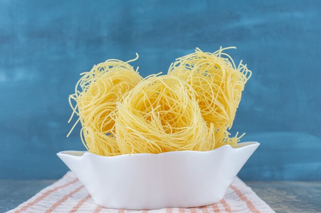 Dünne Spaghetti in der Schüssel auf einem Handtuch auf der Marmoroberfläche.