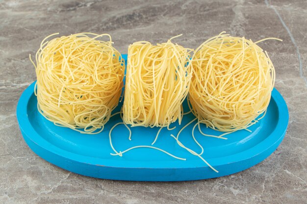 Dünne Spaghetti-Nester auf blauem Teller.