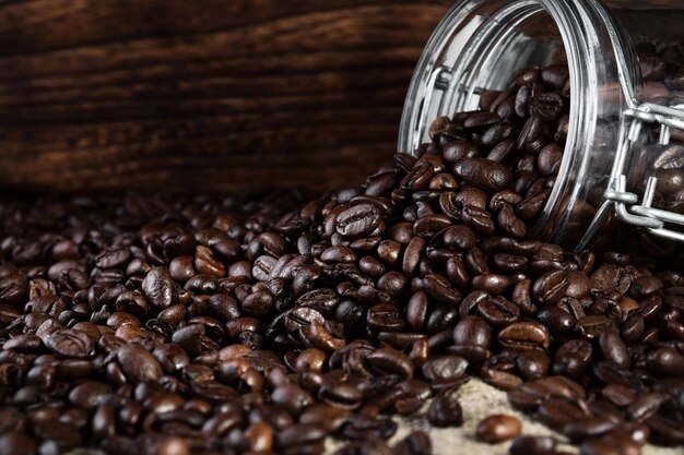 Duftende Kaffeebohnen werden aus einem Glas auf einem rustikalen Tischplattenhintergrund verstreut. Selektiver Fokus der Nahaufnahme Kopieren Sie Platzbanner