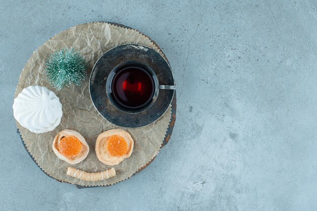 Duftende Tasse Tee, Bündel Desserts und eine Baumfigur auf einem Holzbrett auf Marmor.