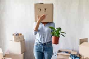 Kostenloses Foto dumme frau, die mit kasten über kopf und pflanze in der hand beim packen aufwirft, um sich zu bewegen