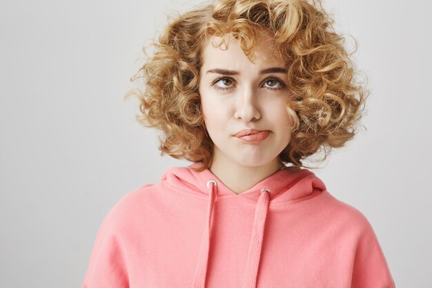 Dummes gelangweiltes Mädchen, das Locken aus den Haaren bläst und blinzelt