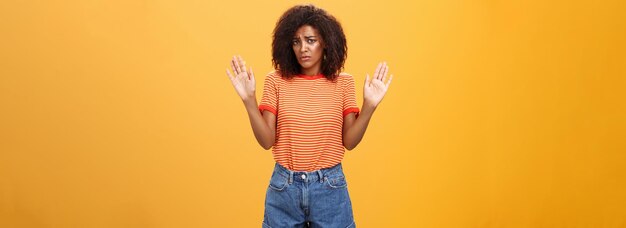 Dummes, unsicheres und trauriges dunkelhäutiges weibliches Model in trendigem gestreiftem T-Shirt und Shorts, das die Arme in