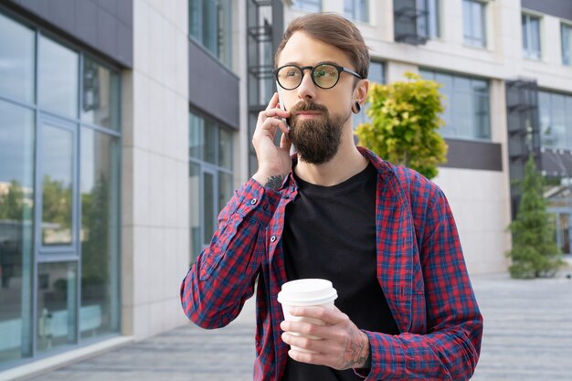 Dunkelhaariger bärtiger Mann in Brille, der über Smartphone spricht