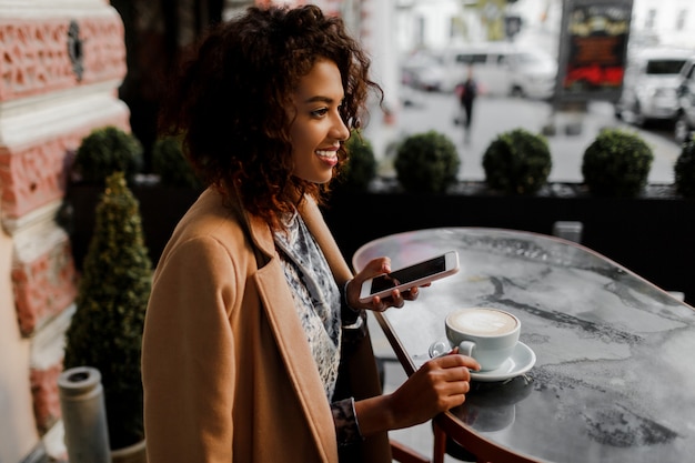 Dunkelhäutige Frau mit Afro-Frisur, die ihren Newsfeed oder ihre Nachrichten über soziale Netzwerke überprüft