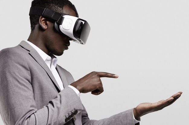 Dunkelhäutiger Mann in Abendgarderobe mit Virtual-Reality-Headset für Smartphone auf dem Kopf, Videospiele spielend.