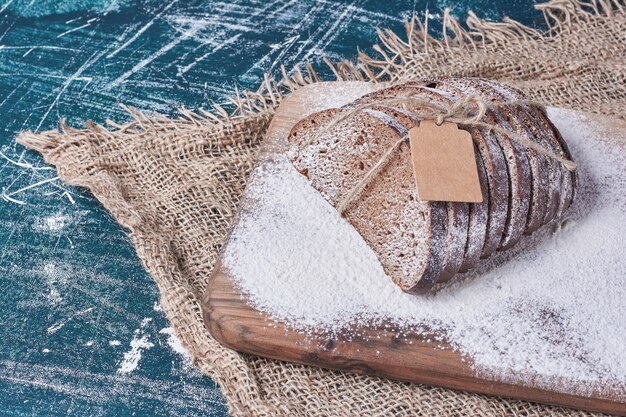 Dunkle Brotscheiben auf Holzbrett auf blauem Tisch.