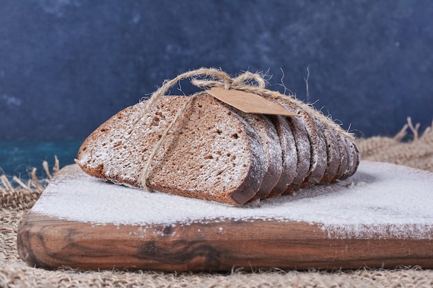 Dunkle Brotscheiben auf Holzbrett auf blauem Tisch.