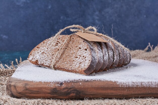 Dunkle Brotscheiben auf Holzbrett auf blauem Tisch.